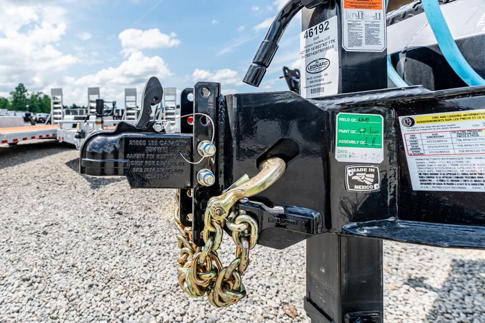 Close-up of a trailer hitch with a chained safety lock securing the coupler and visible labels on the black metal frame.