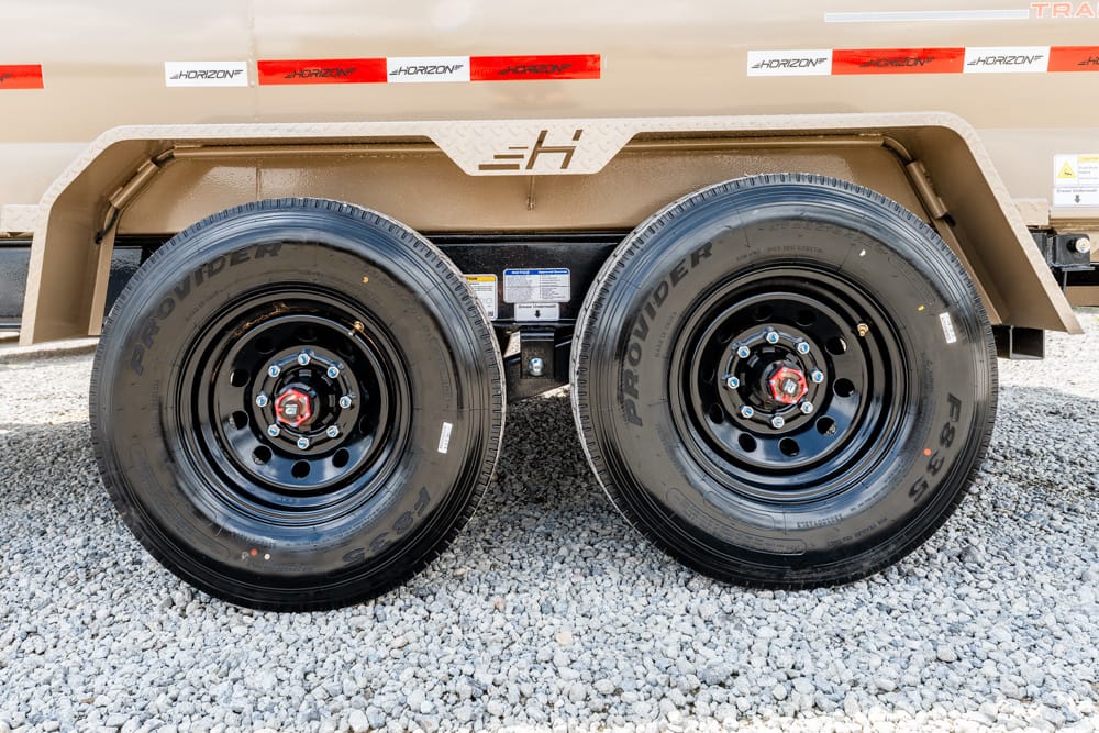 Dual-axle trailer with black steel rims and red lug nuts on a gravel surface