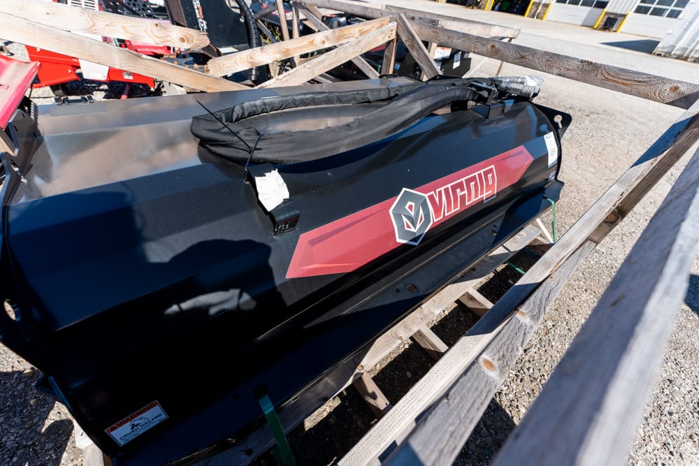 Large black industrial fuel tank with a red diagonal stripe and logo, strapped inside a wooden crate in an outdoor gravel lot.