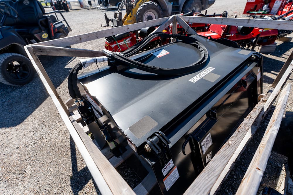 Large black industrial battery inside a wooden crate outdoors, with thick cables connected to it on a gravel surface among machinery.