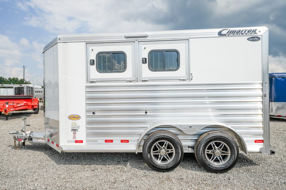 White aluminum horse trailer with two small windows and dual wheels on a gravel lot, side view