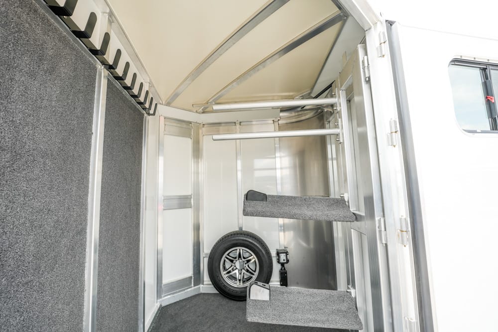 Interior of a metal trailer with carpeted folding stairs, a spare tire on the floor, and wall-mounted storage racks