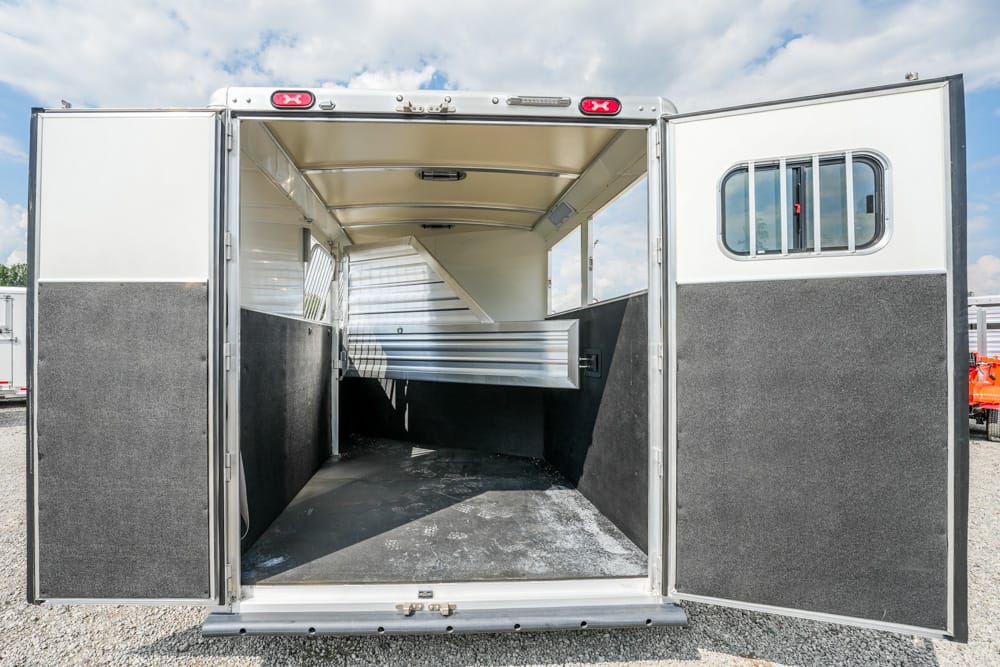 Open horse trailer interior with partition and rubber flooring, doors wide open to daylight, ready for loading.