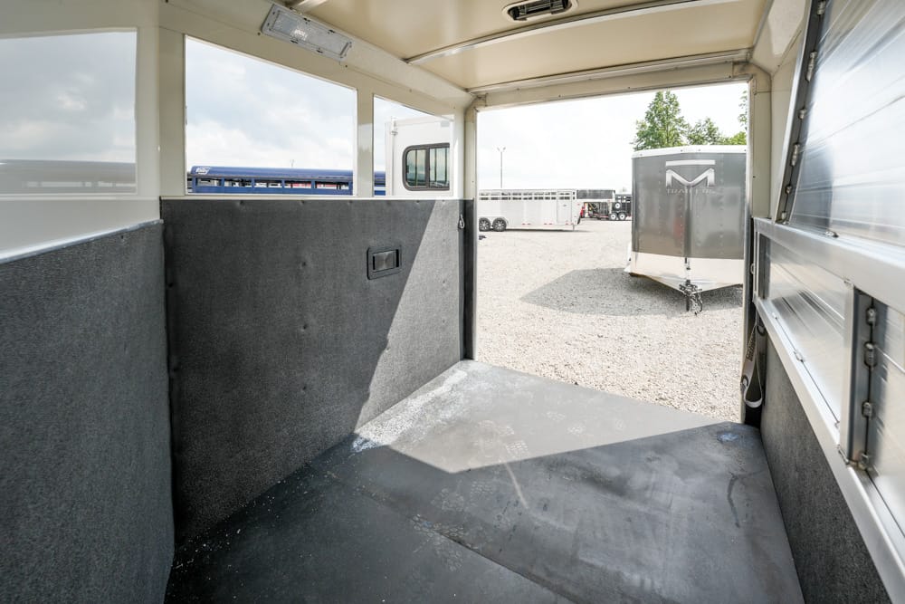 Interior of an empty utility trailer with padded gray walls and an open back door to a gravel trailer yard outside.