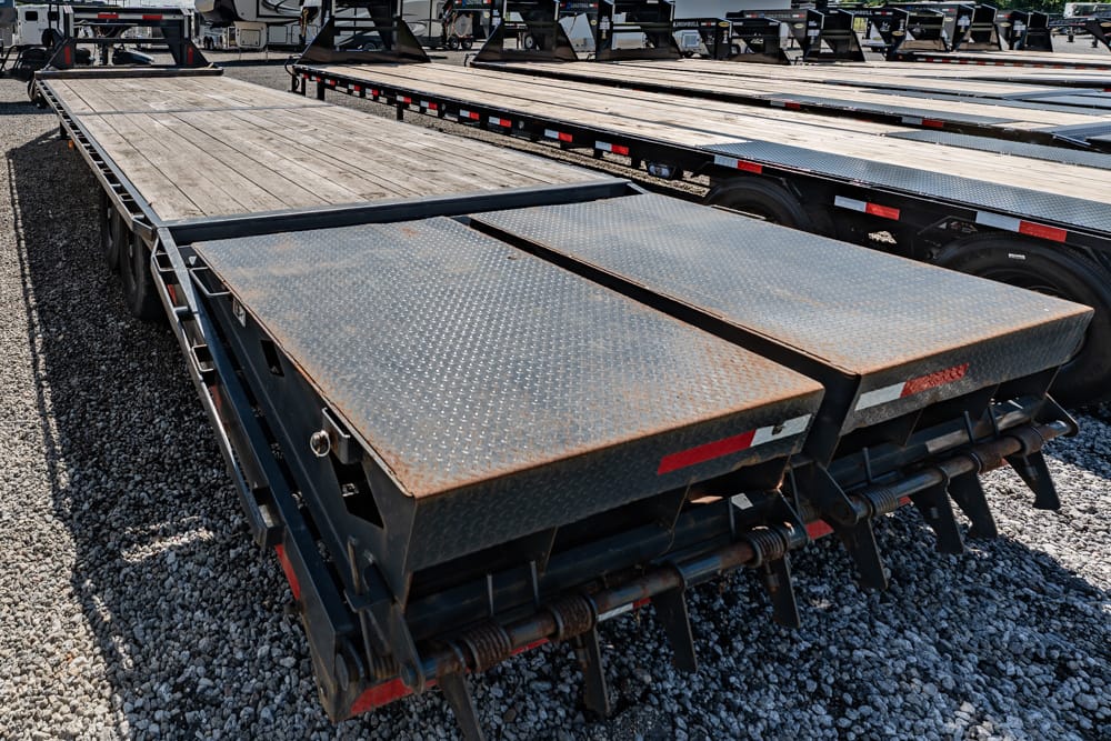 Close-up of rusted diamond-plate ramps on a flatbed trailer in a gravel lot
