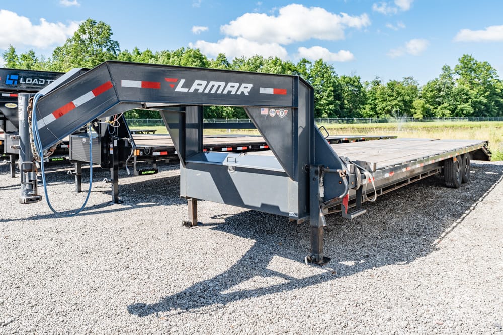 Flatbed trailer with a raised gooseneck, Lamar branding, parked on gravel in an outdoor lot.