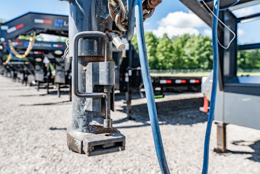 Close-up of a rusty padlock securing a trailer hitch on a metal post, with blue cables and a row of trailers in the background.