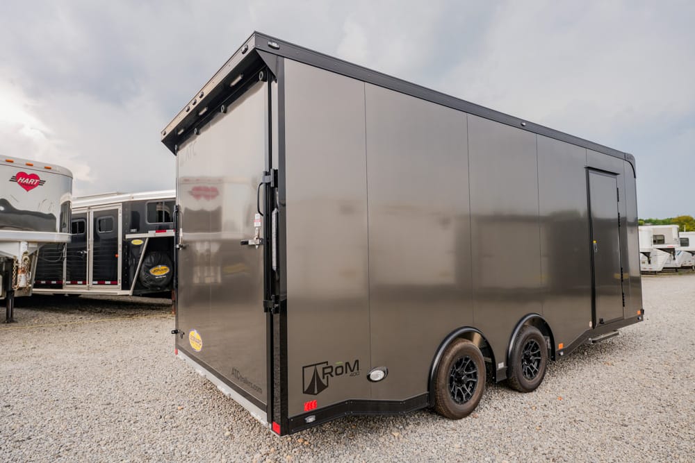 Large black enclosed cargo trailer with dual axles parked on a gravel lot, with other trailers in the background.