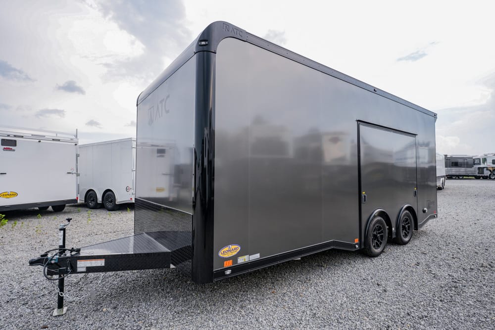 Gray enclosed cargo trailer with a front hitch and dual axles on a gravel lot.