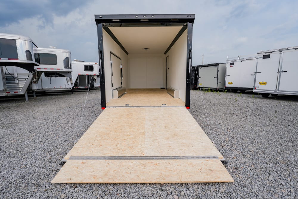 Open cargo trailer with ramp lowered to a gravel lot, ready for loading, surrounded by other trailers.