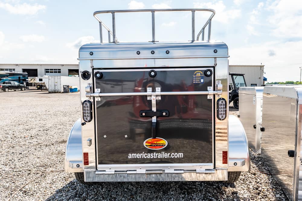 Rear of a polished aluminum trailer with a large central door, chrome hardware, and the text 'americatrailer.com' on the door.