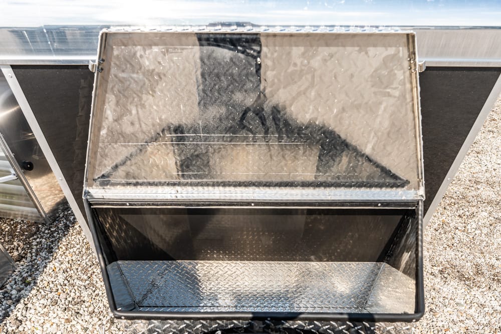 Open metal storage chest with diamond-plate interior on gravel surface.