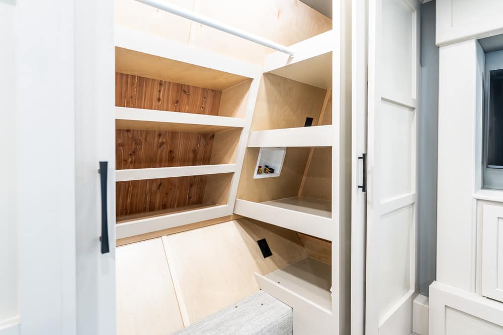 White built-in closet with angled shelves and light wood interior; mostly empty storage space.