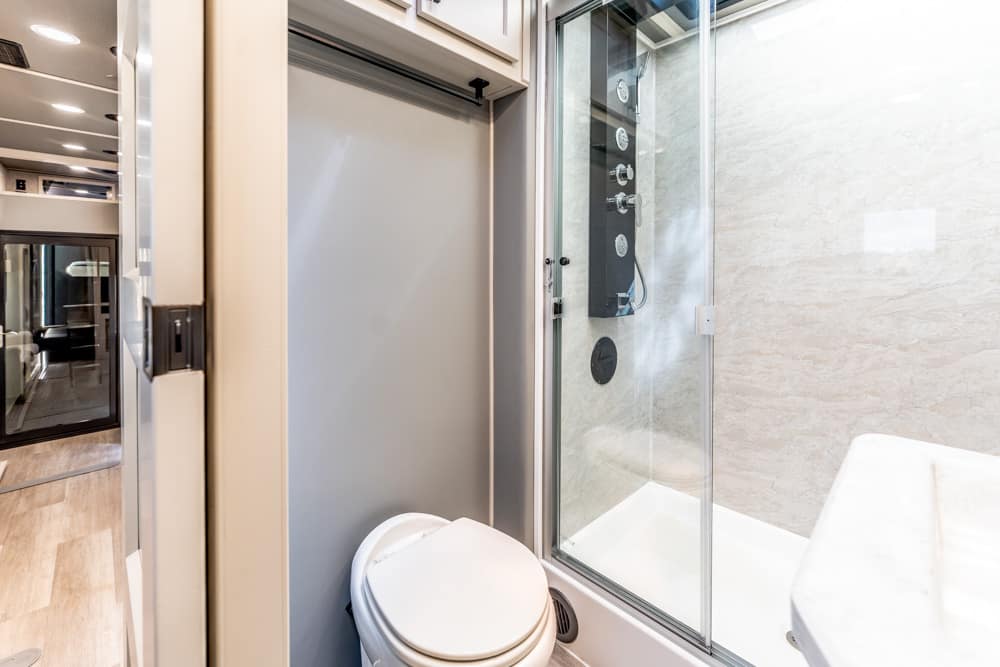 Compact bathroom in a modern RV or trailer featuring a white toilet beside a glass-enclosed shower