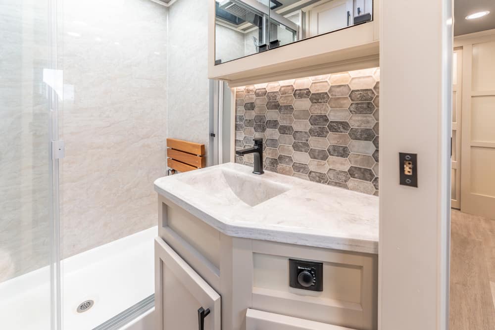 Bathroom vanity with hex tile backsplash, gray countertop, black faucet, and a glass-enclosed shower to the left.