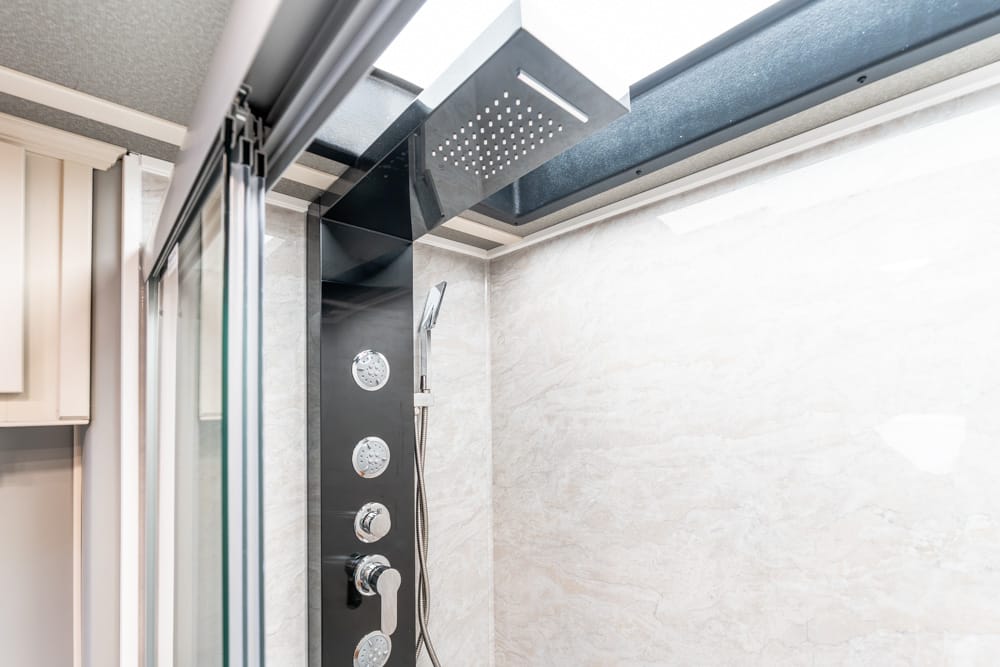 Modern shower panel with multiple body jets and handheld shower head inside a glass-enclosed bathroom.