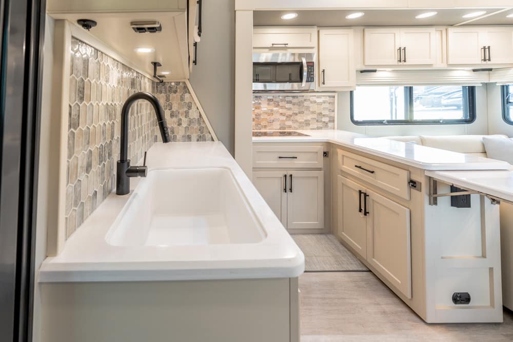 Modern RV kitchen with white cabinets, gray hex tile backsplash, and a white undermount sink with a black gooseneck faucet.