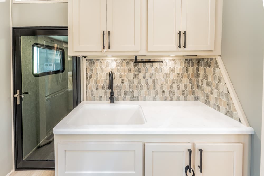 Compact kitchen sink area with white countertop, black faucet, and beige hexagonal tile backsplash.