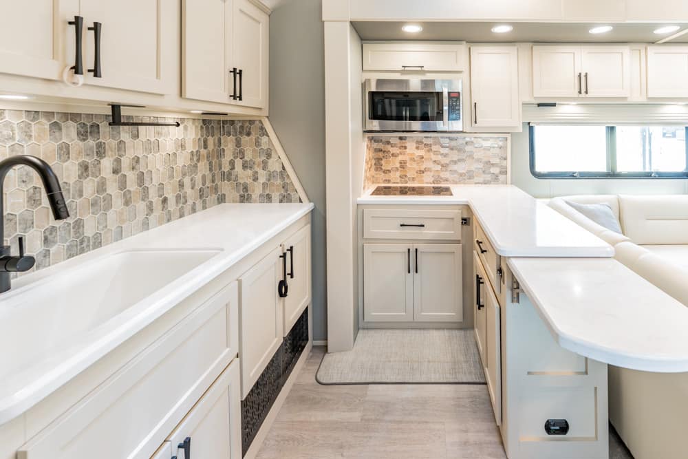 Bright white kitchen in a spacious RV with marble counters, hex tile backsplash, and an island.