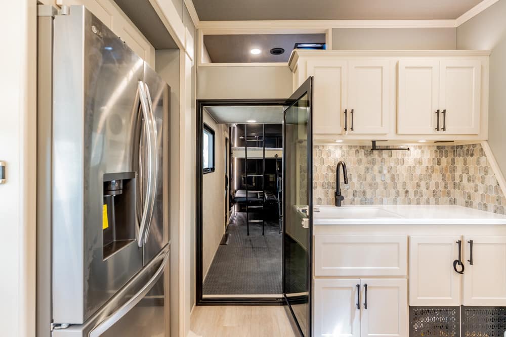 Stainless steel refrigerator beside white cabinets and a hex tile backsplash in a compact kitchen, doorway opening to a hallway.','Open doorway from a modern kitchen to a hallway, showcasing a black faucet, white counters, and a hex tile backsplash.','Modern kitchen with a stainless fridge on the left, white cabinets, and a glass door leading to a living area beyond.