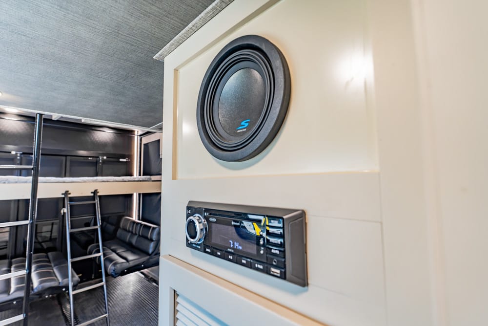 Large circular speaker embedded in a beige wall beside a car stereo unit inside a vehicle cabin.