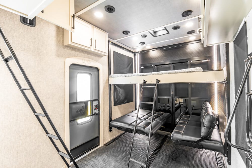Interior of a vehicle's sleeper cabin with two-tier bunks, ladders, and black leather seating along the walls.