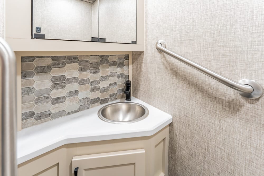 Compact bathroom sink area featuring a small stainless basin, light countertop, hex tile backsplash, and a wall-mounted grab bar for accessibility.