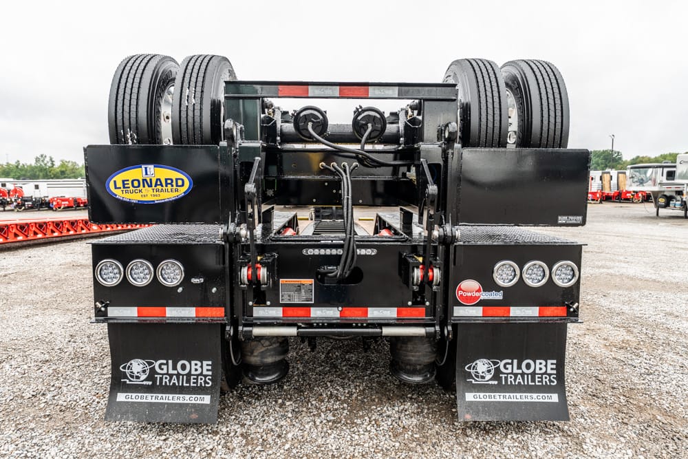 Rear view of a black Globe Trailers semi-trailer with dual rear axles, exposed hydraulics, and hoses in the center; branding stickers visible (Leonard, Globe Trailers).