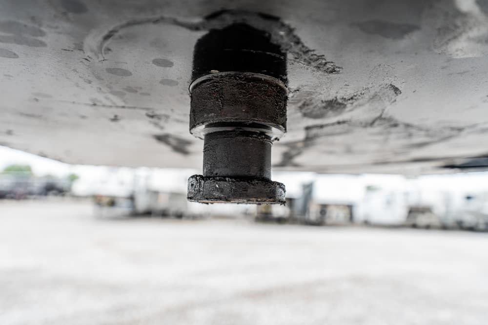 Close-up of a rusted trailer hitch bolt under a boat trailer, with the yard blurred in the background.