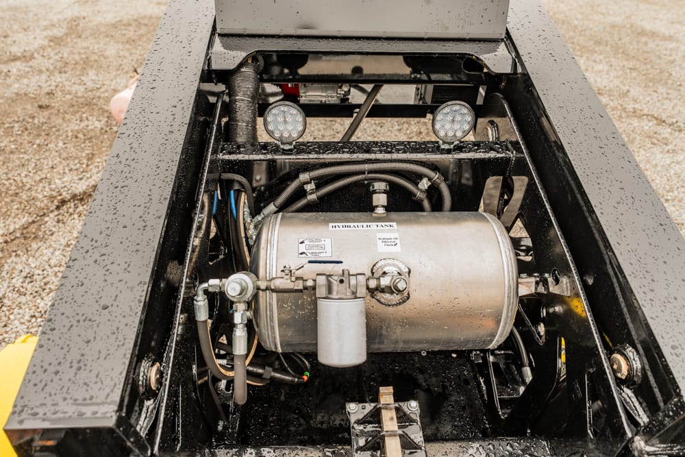 Close-up of a hydraulic tank and hoses inside a metal chassis of industrial equipment, with moisture on surfaces and two round LED lights above.