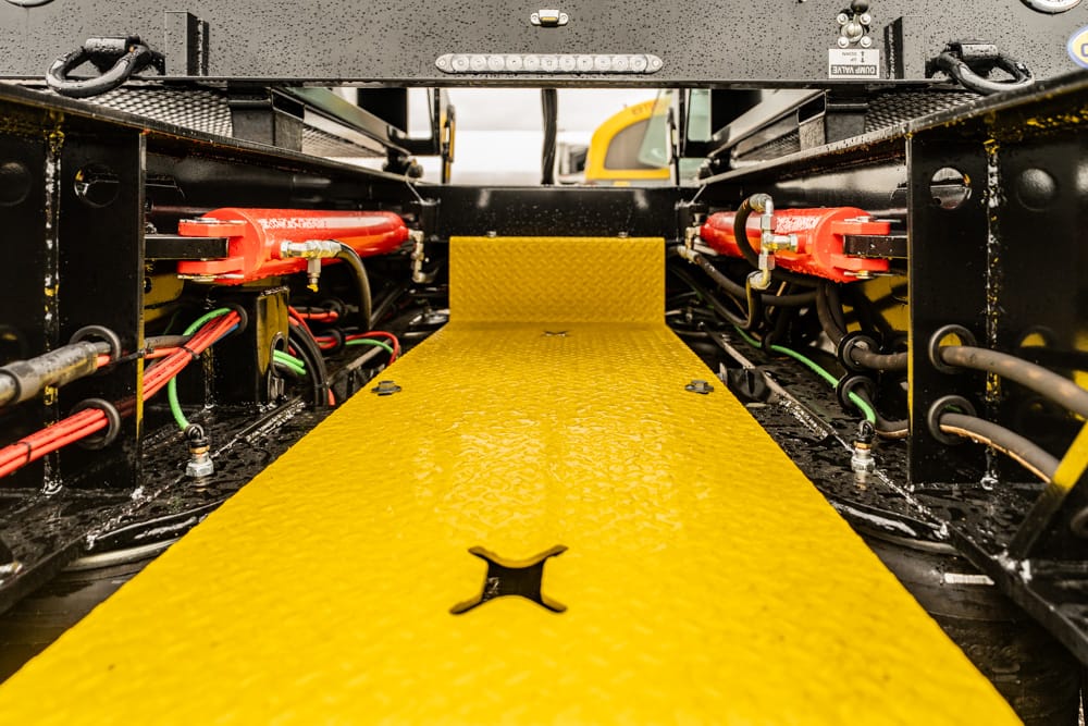 Bright yellow textured service ramp inside a vehicle chassis, flanked by red clamps and various cables and hoses on black metal frames.