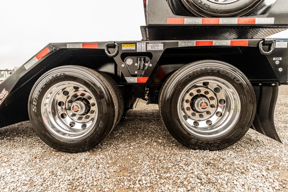 Close-up of dual truck wheels with polished chrome rims on a heavy-duty trailer, parked on gravel.