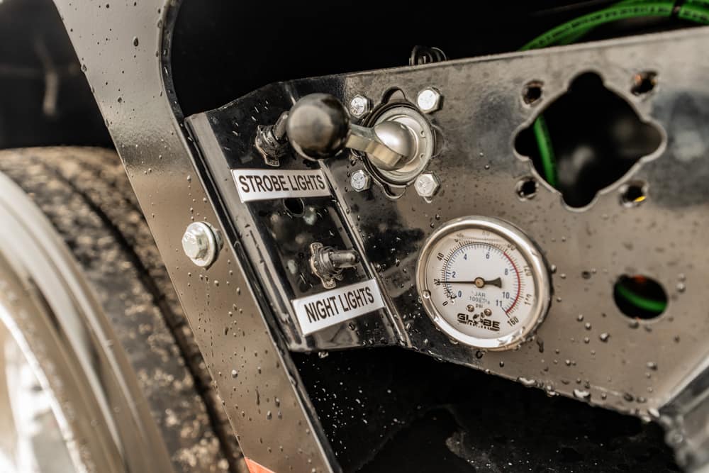 Control panel on a metal vehicle with switches labeled 'Strobe Lights' and 'Night Lights' and a nearby circular gauge.