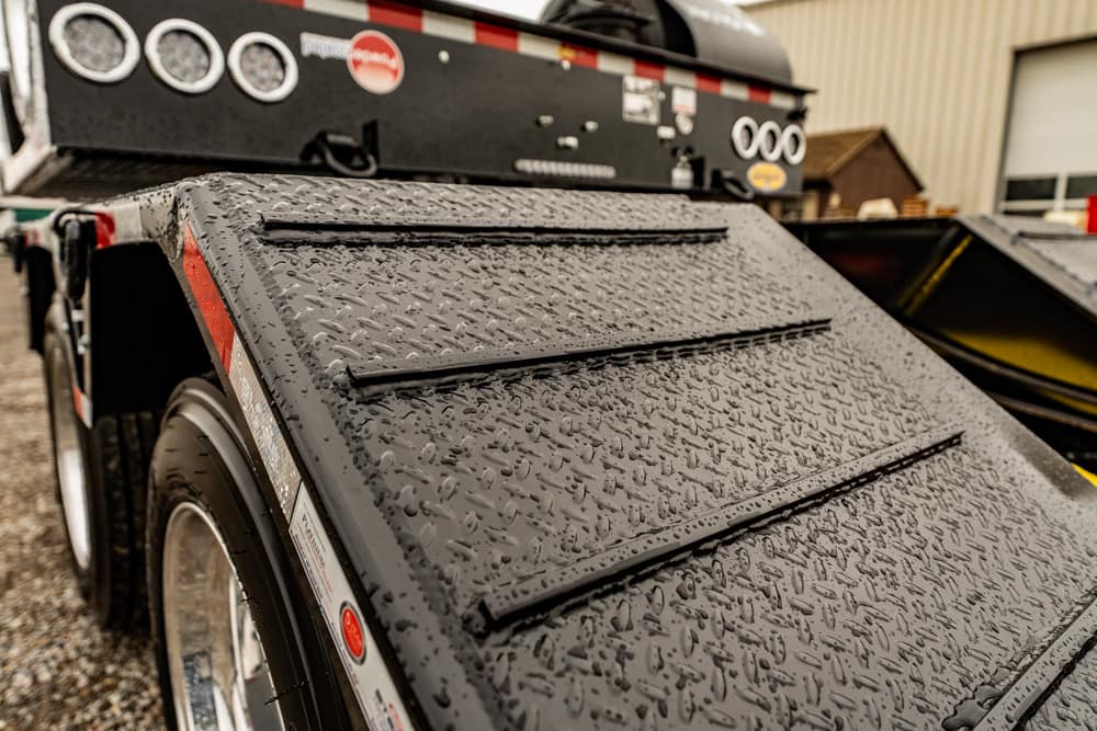 Wet diamond-plate ramp attached to a black trailer, with a tire visible nearby.