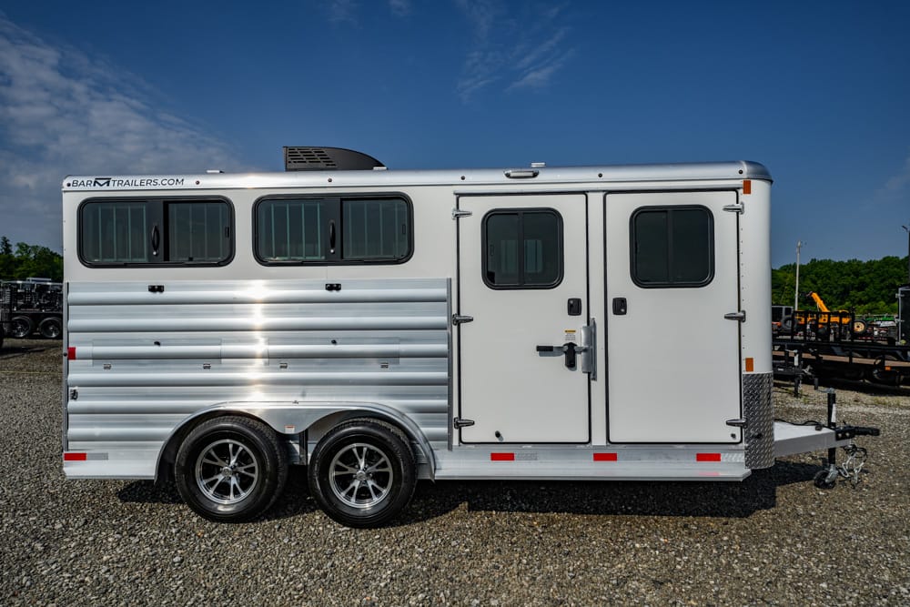 Silver aluminum horse trailer with two compartments and three side windows on a gravel lot, hitch at the front] ,