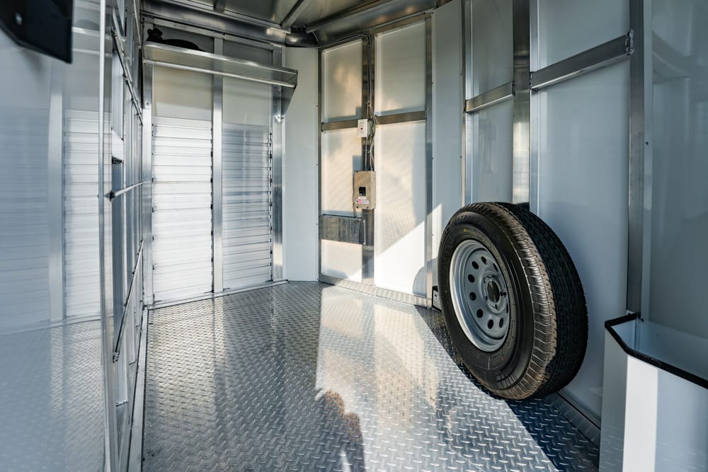 Interior of a silver cargo trailer with a mounted spare tire on the right and a diamond-plate floor.