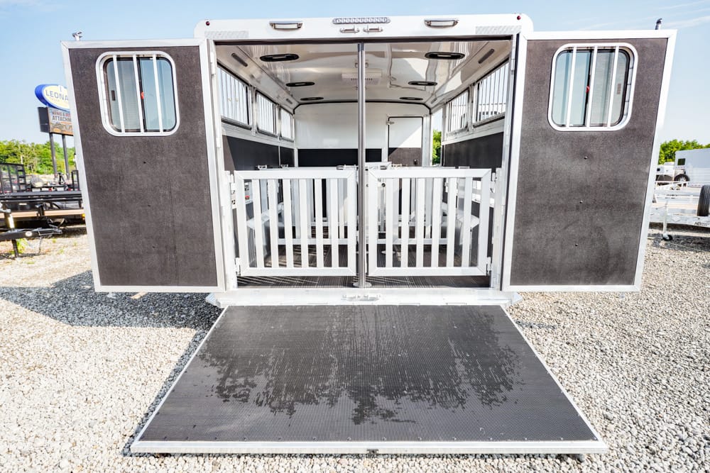 Rear view of a horse trailer with double doors open and a lowered ramp, showing interior stalls.