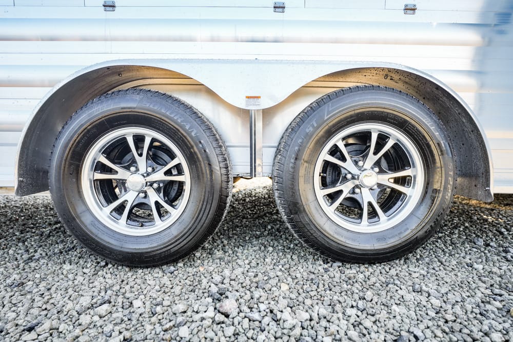 Dual-axle trailer with two black tires and silver rims on a gravel surface