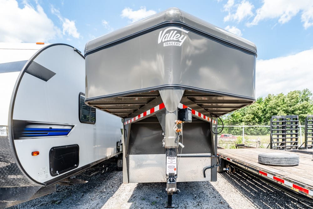 Gooseneck trailer with Valley Trailers branding, attached to its hitch and parked beside a white travel trailer in a gravel lot.