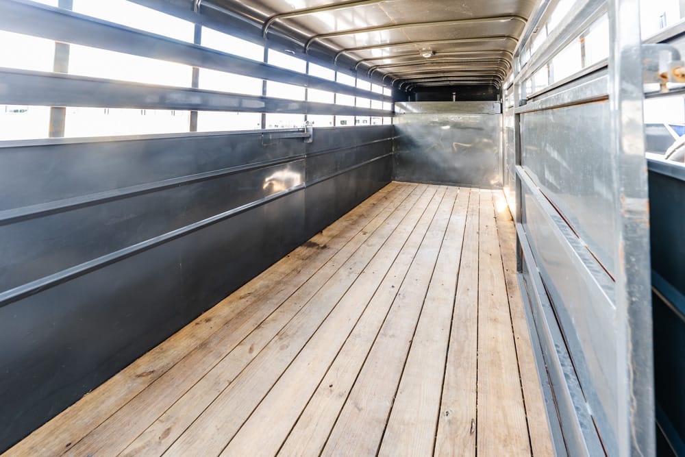 Interior of an empty metal truck trailer with a wooden plank floor and high side rails, cargo space visible from the back gate perspective.