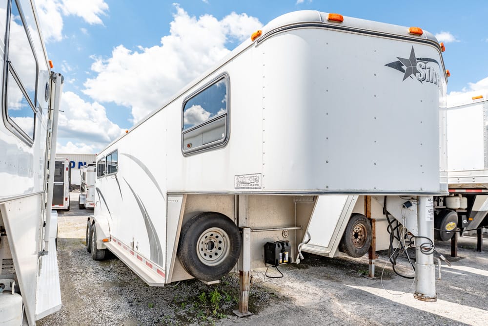 White travel trailer with a raised front section parked on a gravel lot, with other trailers nearby and a blue sky above.