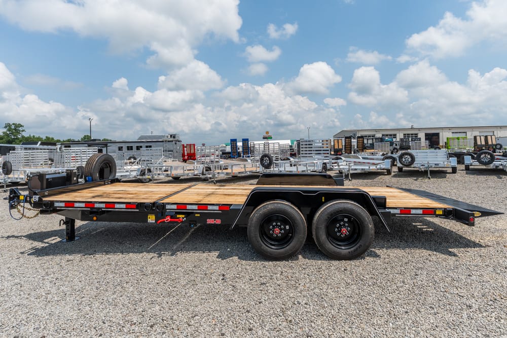 Flatbed trailer parked on a gravel lot with other trailers in the background under a blue, cloudy sky.