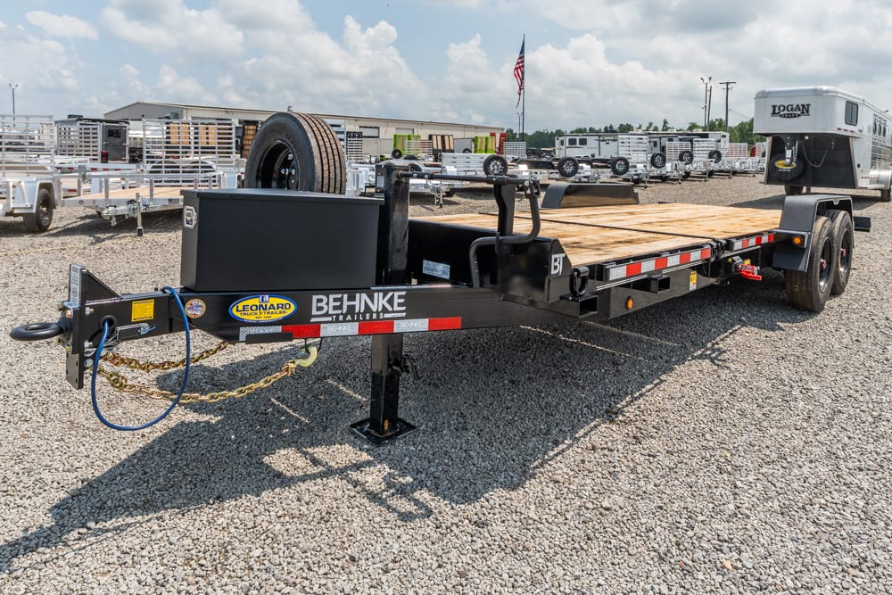 Behnke flatbed trailer with a wooden deck, parked on a gravel lot; logo visible on the frame.