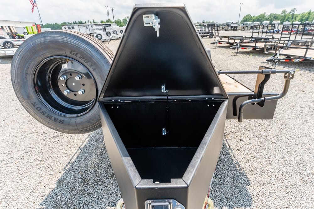 Open, triangle-shaped metal storage box on a trailer with a spare tire mounted to the left, set on a gravel lot.