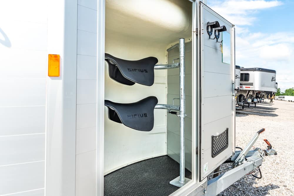 Open rear of a white trailer showing a saddle rack with two black saddles mounted on a vertical post.