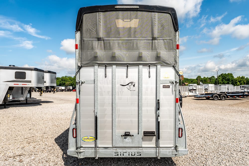 Rear view of a silver Sirius horse trailer in a gravel lot, with a black canopy and blue sky.