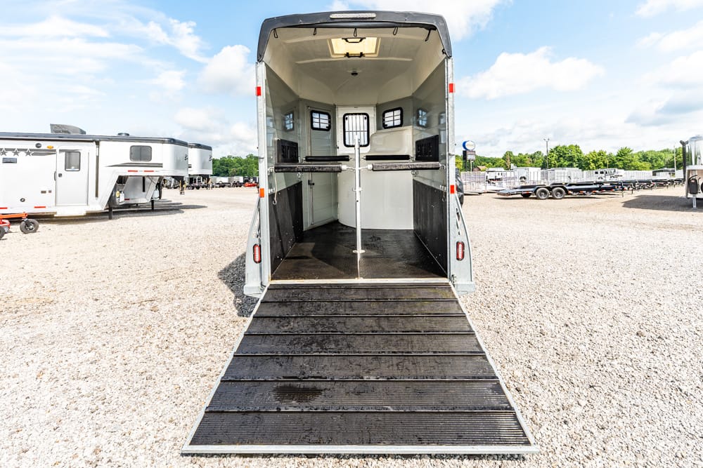 Open horse trailer with ramp down in a gravel lot, showing interior divider stalls.