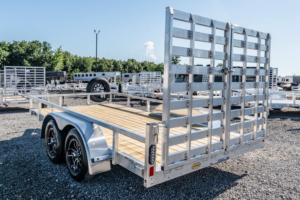 Dual-axle utility trailer with a wooden bed and tall metal gate in a gravel trailer yard.
