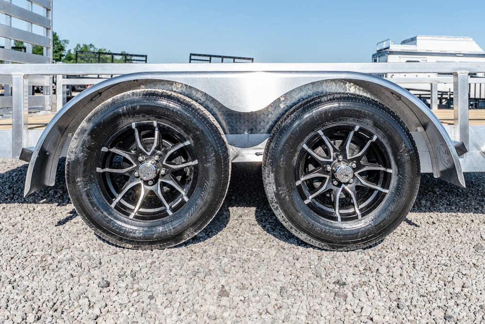Dual-axle boat trailer with black alloy wheels on a gravel surface