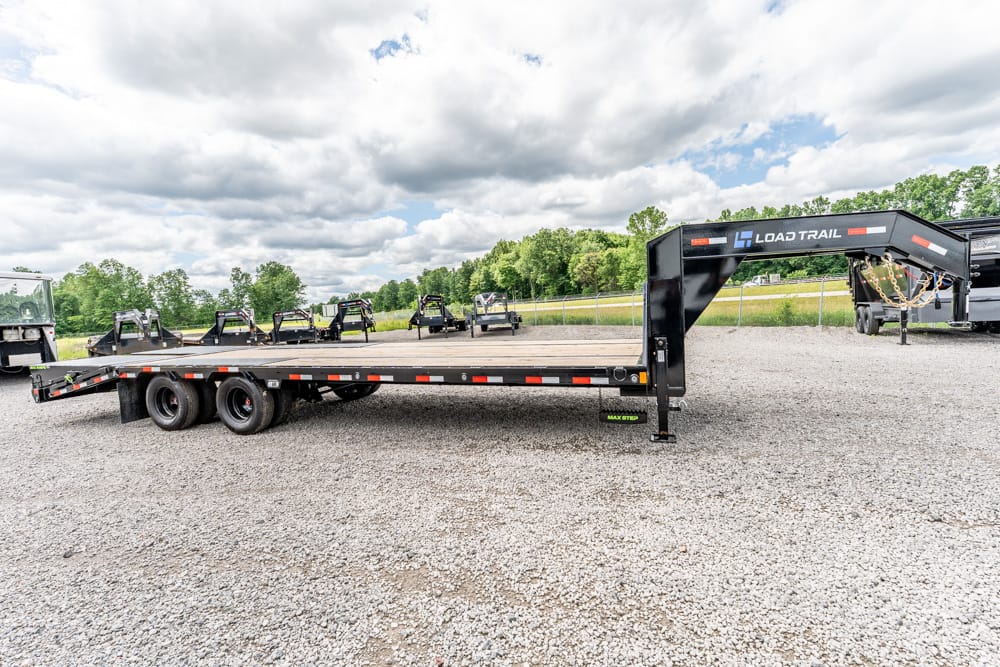 Black Load Trail gooseneck flatbed trailer with dual rear axles on a gravel lot, empty deck ready for hauling